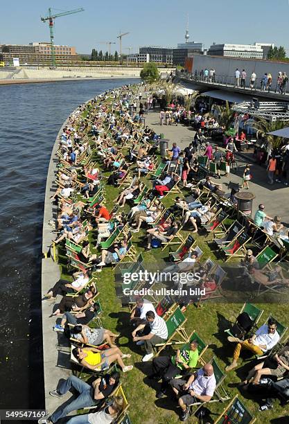 People lie on deck chairs at the bank of the river Spree near Hauptbahnhof railway station in Berlin on a sunny day in May