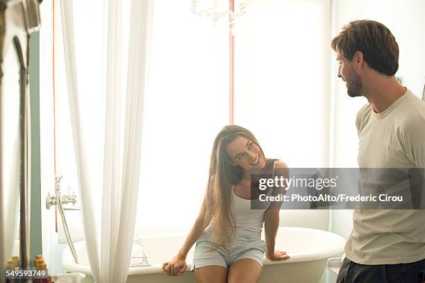 woman sitting on bathtub edge giving husband suggestive look - bad relationship stockfoto's en -beelden