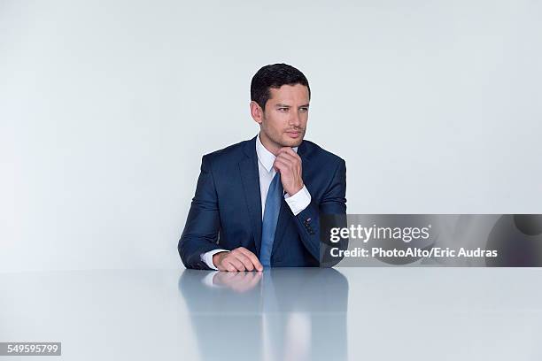 businessman seated at table, looking away in thought - hand on chin thinking stock pictures, royalty-free photos & images