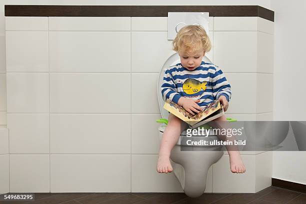 Year old boy with childrens seat and childrens book on a toilet.