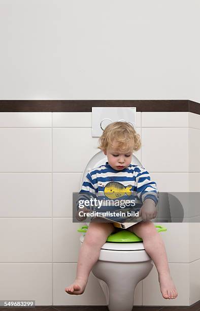 Year old boy with childrens seat and childrens book on a toilet.