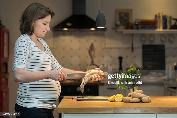 Pregnant woman, 35 years, cooking a fresh trout in the kitchen.