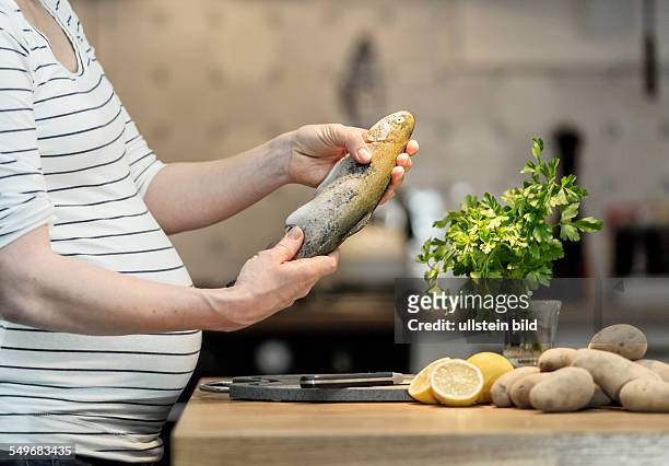 Pregnant woman, 35 years, cooking a fresh trout in the kitchen.