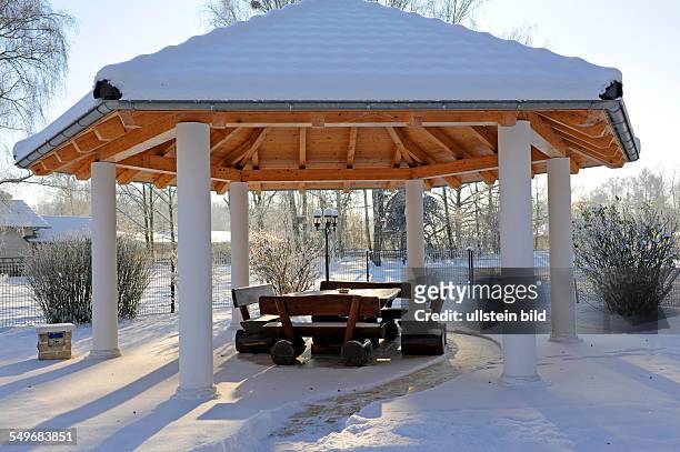 Winterlicher Landhausgarten mit Pavillon und rustikaler Sitzgruppe, schneebedeckt