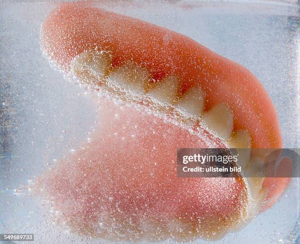 Ein Zahnersatz wird in einem Glas mit Wasser gereinigt. Richtige Hygiene.