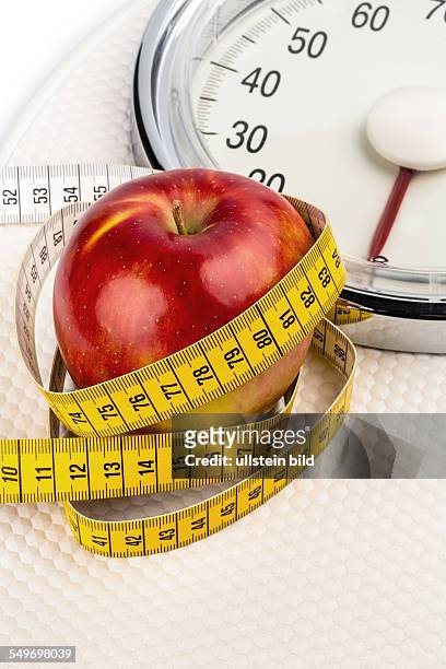 Auf einer Personenwaage liegt ein Apfel. Symbolfoto für Abnehmen und gesunde, vitaminreiche Ernährung.