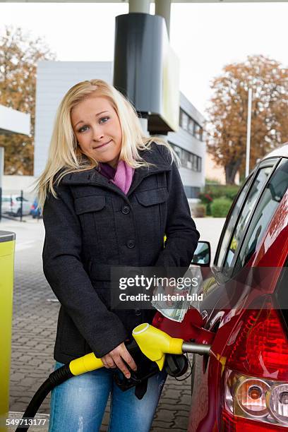 Eine junge Frau Tankbenzin auf einer Tankstelle. Die Kosten für das Auto werden wegen der Benzinpreise immer teurer