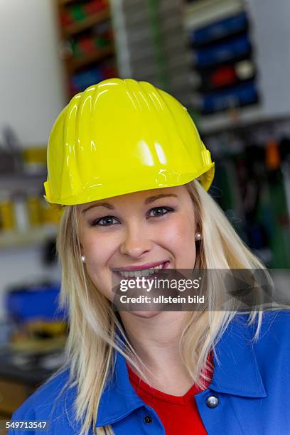 Junge Mechanikerin mit gelben Helm und Schraubenschlüssel in einer Werkstatt. Seltene Frauenberufe.