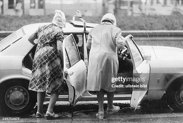 Berlin, Taxi; zwei alte Frauen steigen bei Regen in ein Taxi