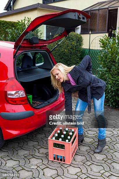 Eine junge Frau hebt eine Kiste mit Flaschen aus ihrem Auto. Richtiges Leben verhindert Rückenschmerzen und Bandscheibenvorfall