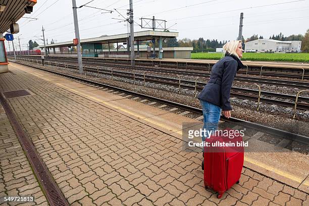 Eine junge Frau mit Koffer wartet auf dem Bahnsteig eines Bahnhofes auf ihren Zug. Zugverspätungen