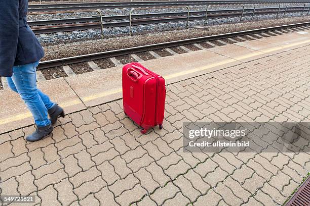 Eine junge Frau mit Koffer wartet auf dem Bahnsteig eines Bahnhofes auf ihren Zug. Einsame Gepäckstücke auf Bahnhöfen sind gefährlich