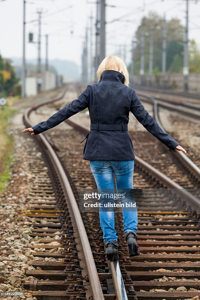 Auf der Suche nach der richtigen Entscheidung balanciert eine junge Frau auf einem Gleis. Das Leben stellt die Weichen.