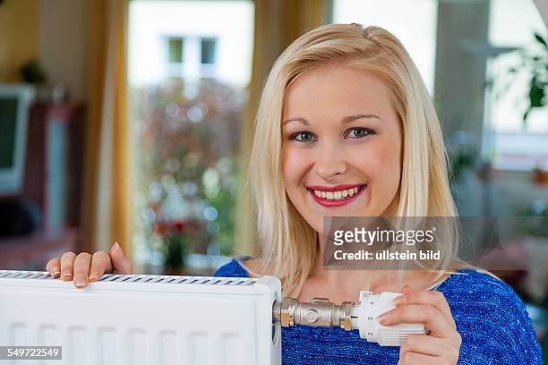 Zum Sparen von Energie und Strom senkt eine junge Frau die Temperatur im Wohnraum