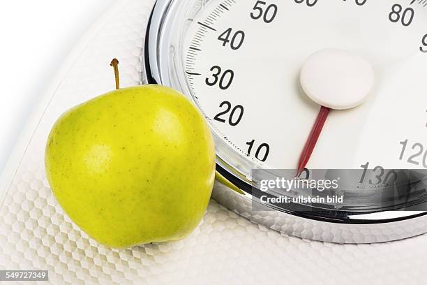 Auf einer Personenwaage liegt ein Apfel. Symbolfoto für Abnehmen und gesunde, vitaminreiche Ernährung.