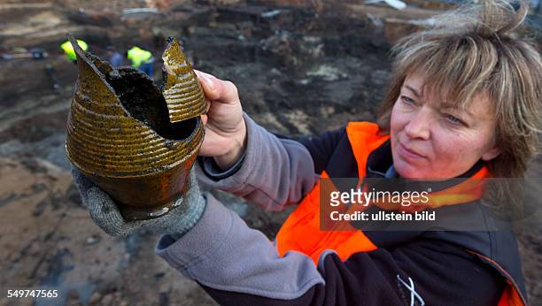 Grabungsleiterin betrachtet ein Gefaess aus glasierter roter Irdenware vor der Ausgrabung der grossflaechigen Holzlage aus der Zeit vor 1250 in der...