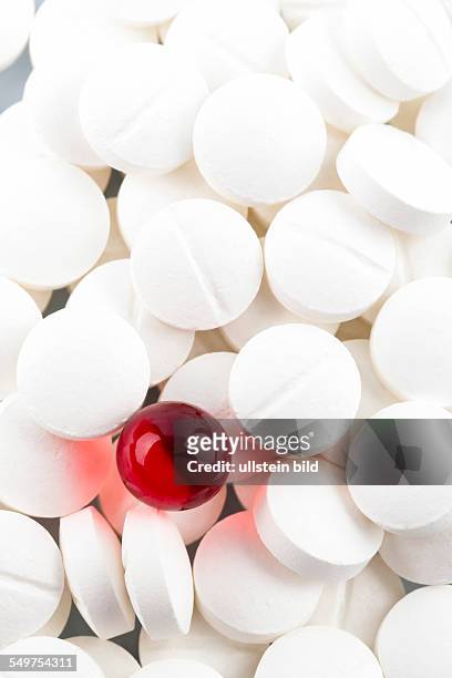 Weiße Tabletten im Kontrast mit einer roten Tablette, Symbolfoto für Mobbing und Individualität