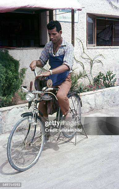 Spanien, ca. 1958, Scherenschleifer auf einem Fahrrad, das den Schleifstein zum schleifen dreht