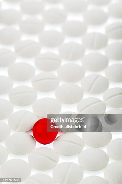 Weiße Tabletten im Kontrast mit einer roten Tablette, Symbolfoto für Mobbing und Individualität