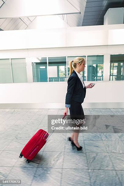 Eine Geschäftsfrau mit Koffer und Smartphone auf einem Flughafen. Mobilität und Kommunikation bei Geschäftsreisen