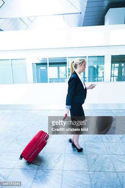 Eine Geschäftsfrau mit Koffer und Smartphone auf einem Flughafen. Mobilität und Kommunikation bei Geschäftsreisen