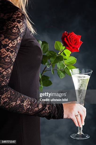 Eine Frau im Abendkleid mit einer roten Rose und einem Glas Sekt oder Champagner