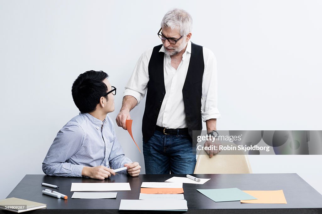 Two men with markers and papers talking