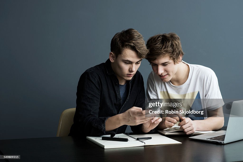 Young men sitting at table looking at calculator