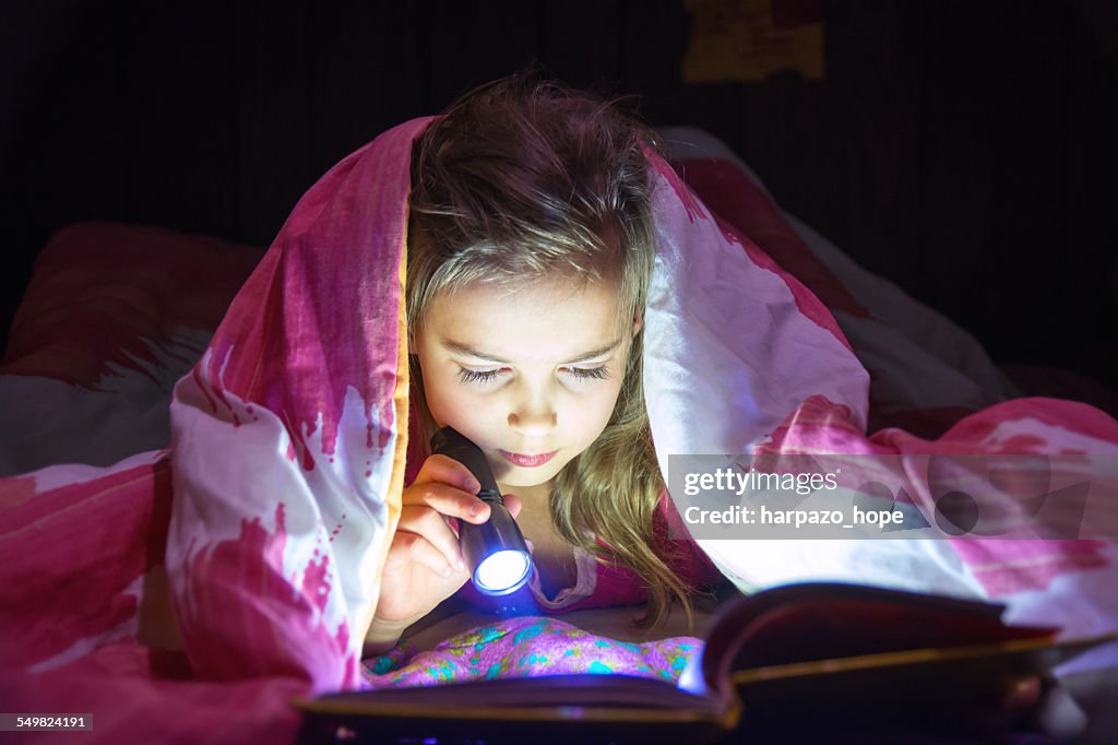 Girl reading with a flashlight.