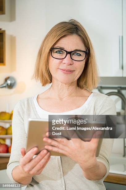 senior woman in kitchen holding digital tablet - alexandra dost stock-fotos und bilder