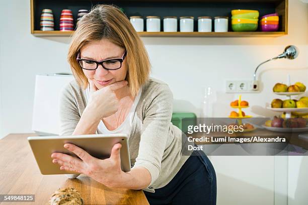 senior woman in kitchen using tablet pc - alexandra dost stock-fotos und bilder