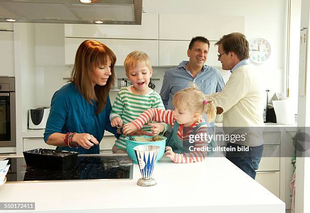 Family Scene: A little boy and a little girl with her mother baking a cake. In the meantime father and grandfather discuss in the kitchen. Aachen