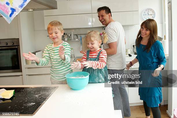 Family Scene: A little boy and a little girl baking a cake together. Father and mother are in the kitchen and watch their children there. Aachen