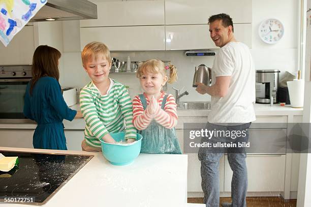 Family Scene: A little boy and a little girl baking a cake together. Father and mother are in the kitchen and watch their children there. Aachen