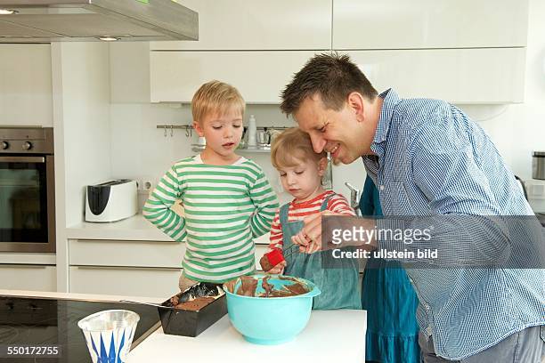 Family Scene: A little boy and a little girl baking with her father a cake in the kitchen. Aachen