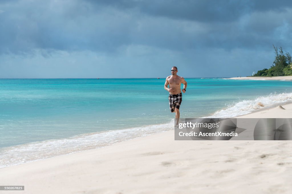 L'uomo corre lungo la spiaggia vuota sul bordo del surf