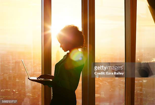 businesswoman on laptop at window in morning sun - leadership stock-fotos und bilder