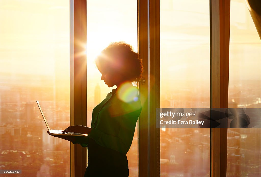 Businesswoman on laptop at window in morning sun