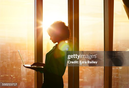 Businesswoman on laptop at window in morning sun Businesswoman on laptop at window in morning sun