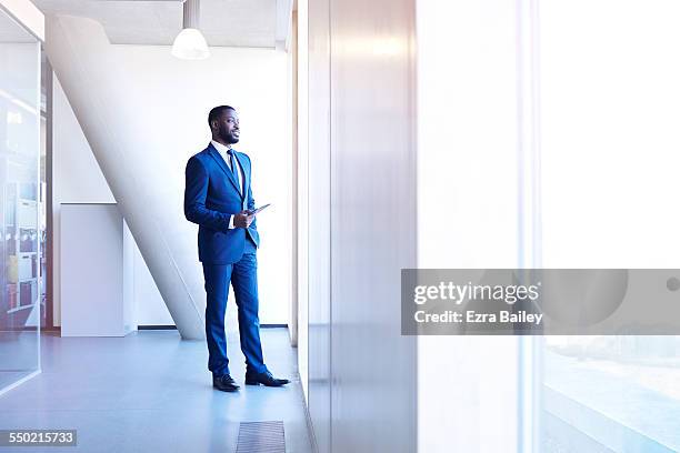 businessman looking out of window holding tablet - blue stock pictures, royalty-free photos & images