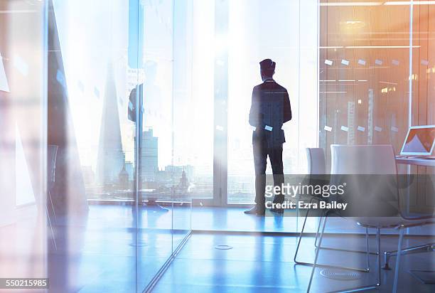 businessman looking out of office over city - foco determinación fotografías e imágenes de stock