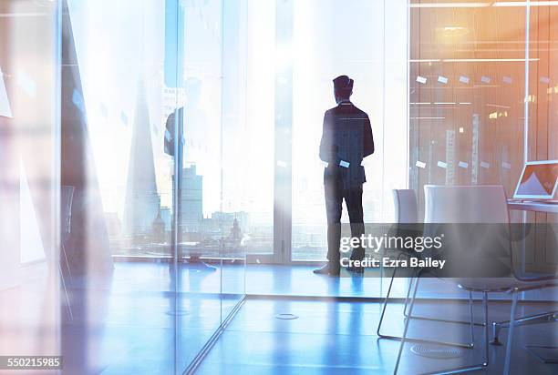 businessman looking out of office over city - looking through imagens e fotografias de stock