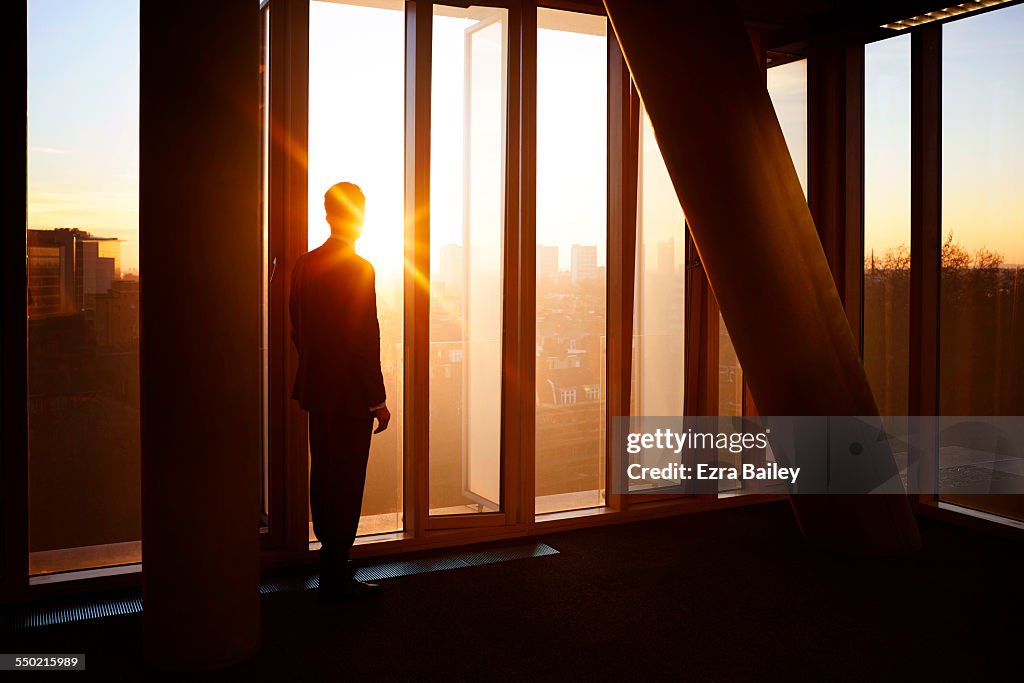 Businessman looks out at city sunrise.