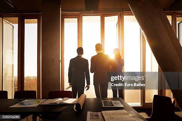 colleagues looking out across city at sunrise - backlit photos et images de collection