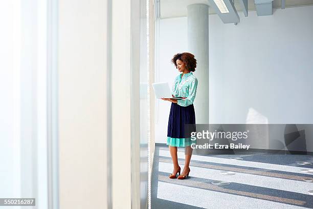 businesswoman with laptop looking out of window - standing with laptop imagens e fotografias de stock