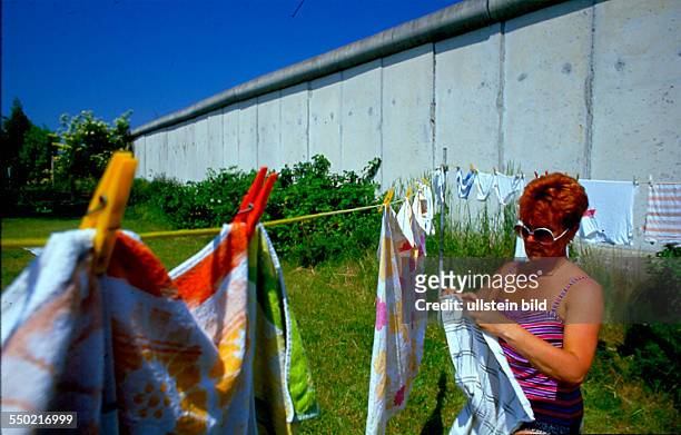 Im Schatten der Mauer: Frau hängt Wäsche auf ihrer Parzelle der Kleingartenkolonie "Freiheit" auf