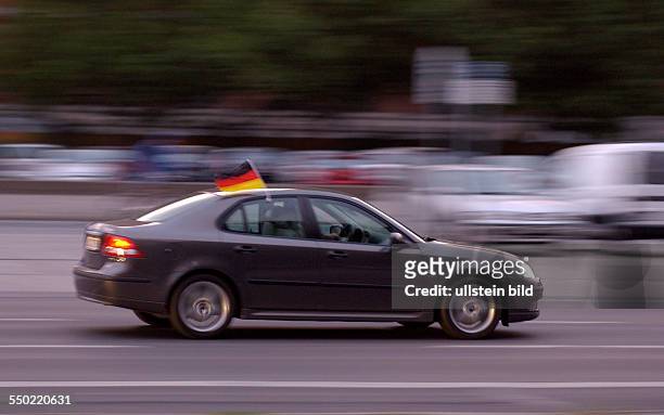 Auto rast mit Deutschlandflagge durch das abendliche Berlin
