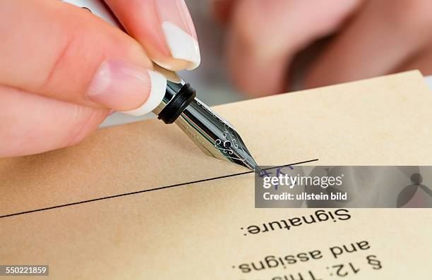 Eine Frau unterschreibt mit dem Füllfederhalter einen Vertrag oder ein Testament.