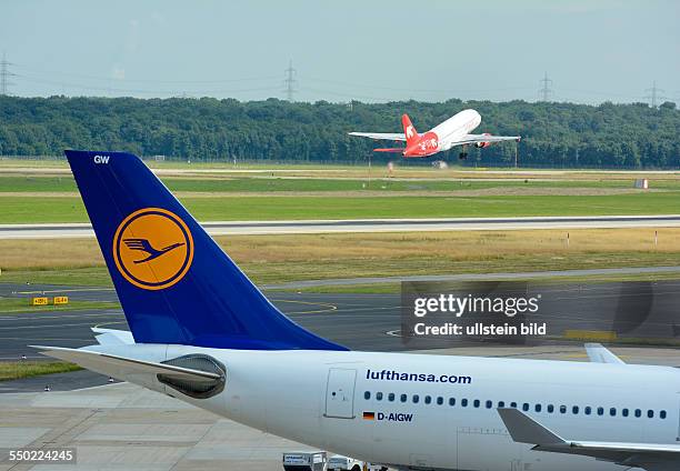 An aircraft of Lufthansa at its parking position while an aircraft of Air Berlin is taking off ; on Duesseldorf airport