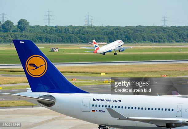 An aircraft of Lufthansa at its parking position while an aircraft of British Airways is taking off ; on Duesseldorf airport